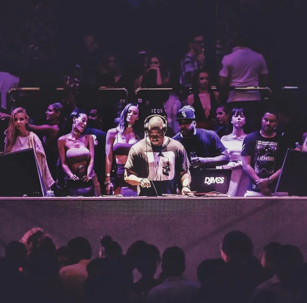 DJ M.O.S. mid-set under purple light with the crowd behind the booth